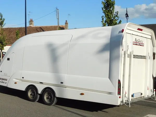 A white hard-shell enclosed car trailer with a rounded nose and a rear loading door